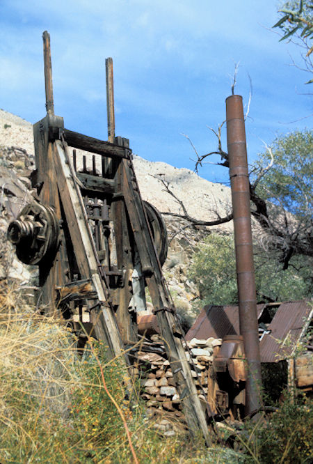 Five stamp mill. Note boiler just to the right and the smoke stack for the boiler which is held upright by guy wires even though it has fallen off the top of the firebox