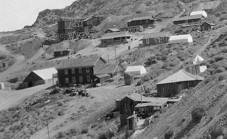 At top just right of center is Lola's dance hall with the girl's cribs below and the roof of the Assay Office just visible. The building below is gone. Slightly below is the Belshaw House with a white tent next to it where the Gordon House was later built in 1909. Center left is the American Hotel with the mule barn to its left. At the bottom right is the Hunter House
