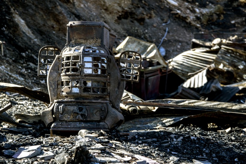 A fire-blackened old stove with broken glass panes and two small doors ajar sits among other charred debris A fire-blackened old stove with broken glass panes and two small doors ajar sits among other charred debris