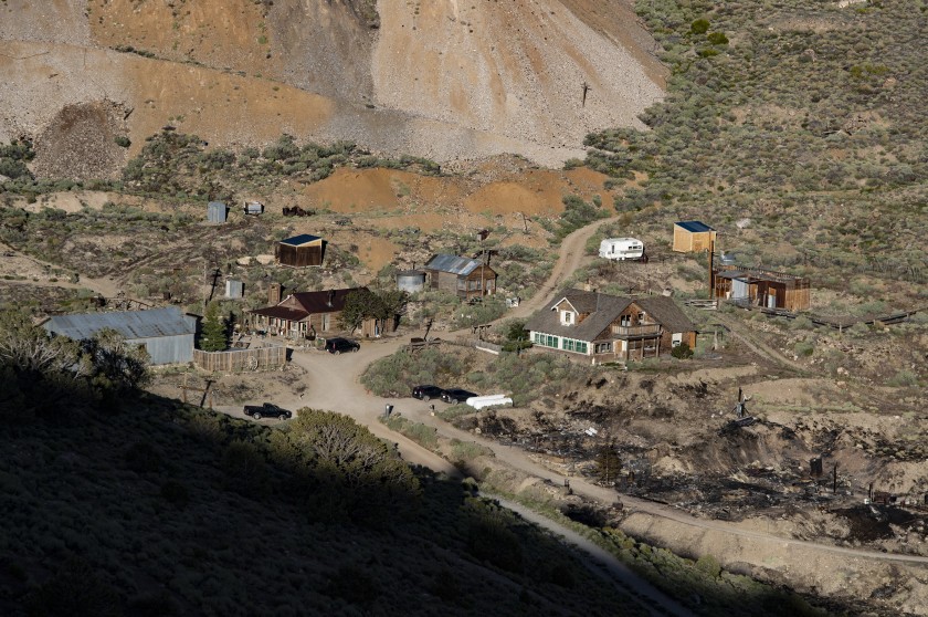 Rustic buildings on a brushy slope below mine tailings near the blackened ground where Cerro Gordo's  American Hotel burned