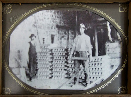 Workers display the 18-inch-long, 85-pound silver-lead ingots that were shipped by wagon from the Cerro Gordo mines to Los Angeles. Photograph hangs on a wall inside the Belshaw House