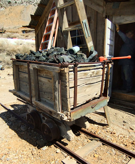 Ore cart, used to haul galena out of the Cerro Gordo mines. On display in the Cerro Gordo mining camp, where it's used as a bin for slag. Behind it, a volunteer is helping to restore the Crapo house